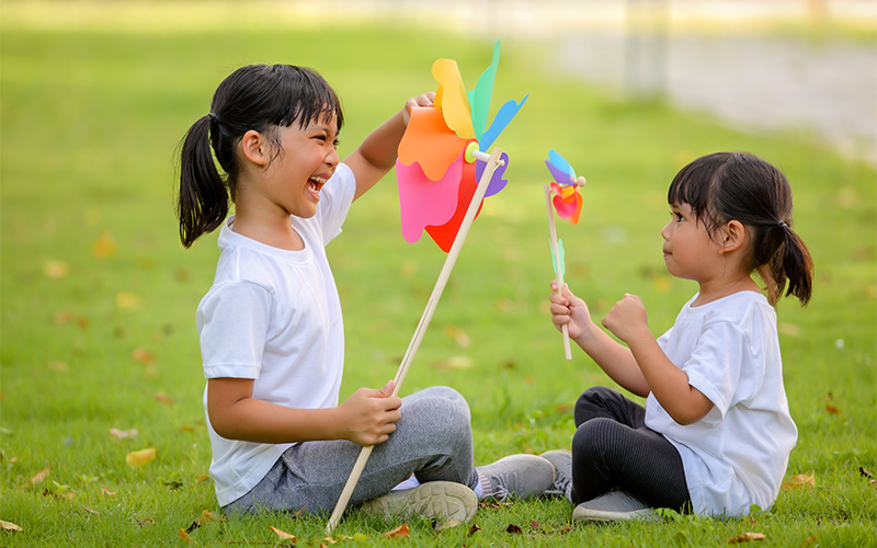 Two happy sisters playing with colorful pinwheels in the park.