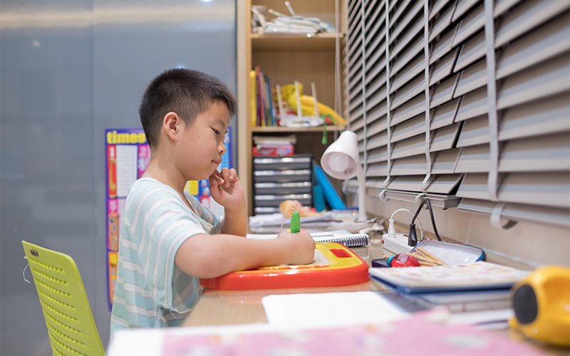  Young boy writing or drawing at his desk for English homework.