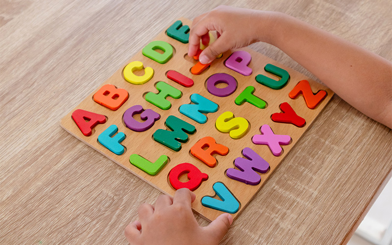 Child’s hands interacting with colorful wooden alphabet puzzle board, placing or removing letter pieces.
