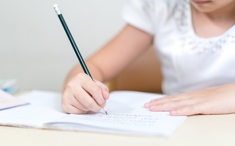 Primary student writing an English essay with a pencil.
