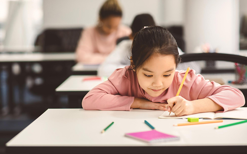Young student focused on writing a PSLE composition draft.