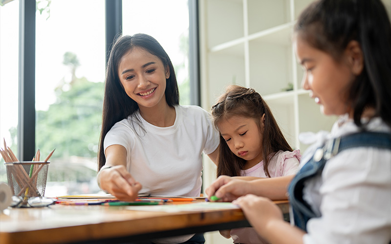 A supportive teacher assisting two young students with a hands-on learning activity