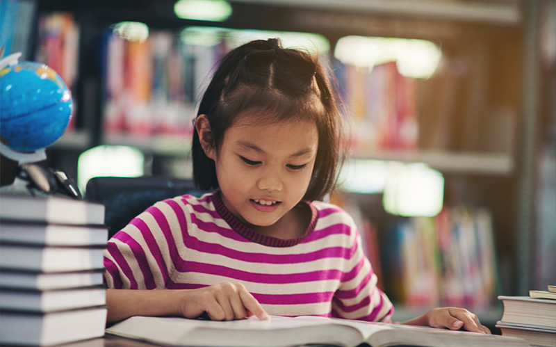 A young girl deeply focused on reading a large book in a library
