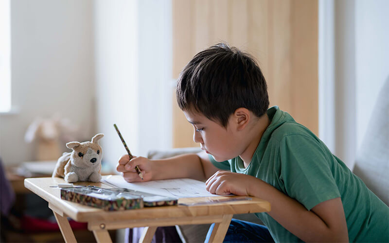 Young child drawing at a small table with a stuffed toy nearby